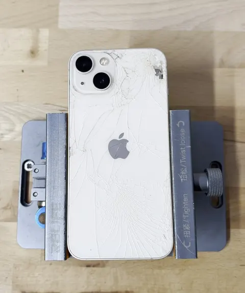 iPhone 13 blanc à la vitre arrière éclatée, sur son support